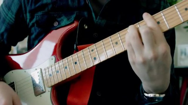 Close up left to right dolly shot of young Caucasian male playing an electric guitar at home. 4k 60 FPS Slow motion. Shot with Blackmagic URSA Mini