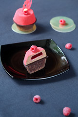 Contemporary Chocolate Raspberry Mousse Cake (the cut) decorated with red velvet spray and caramel elements, on a dark blue background.