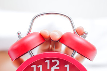 Hand touching turn off red alarm clock on white table