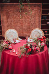 Wedding. Banquet. Marsala. In the forest on a wooden porch is served banquet table with a tablecloth color marsala and vintage chairs. On the table is floral composition and cutlery, glasses, candles