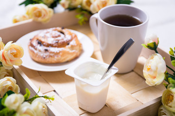 close up of breakfast with bun, yoghurt and tea on wooden tray