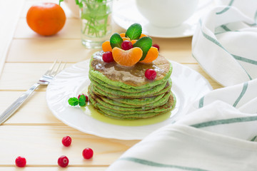 Green pancakes with spinach and bananas decorated citrus, mint and cranberry