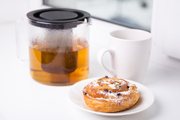 breakfast concept - sweet bun with raisins and cup of tea