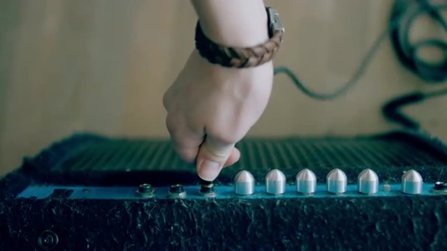 Medium overhead shot of Caucasian male plugging a jack into a guitar amplifier. 4k 60 FPS Slow motion. Shot with Blackmagic URSA Mini