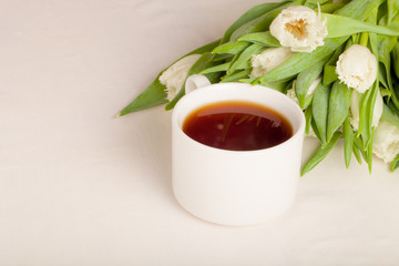 Cup of tea and bunch of spring tulips on the table. Shallow dept