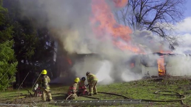 Firefighters use two hoses to spray water on a burning house 