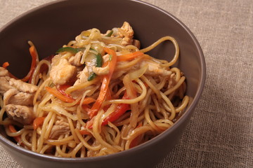 Stir fried noodle with chicken and vegetables in brown plate wit