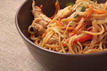Stir fried noodle with chicken and vegetables in brown plate wit
