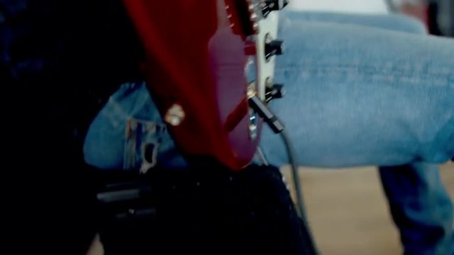 Medium shot of young Caucasian male picking an electric guitar from a stand. 4k 60 FPS Slow motion. Shot with Blackmagic URSA Mini