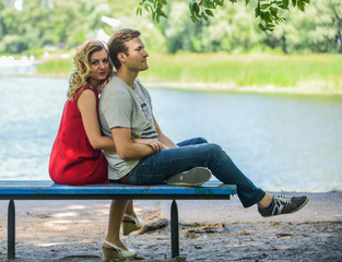 Young and happy couple sitting on the bench hugging. River background