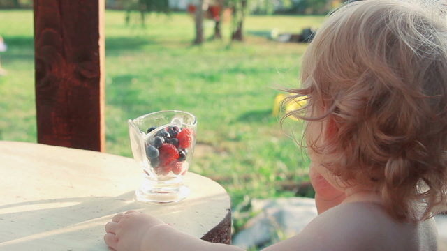 Little girl eating raspberries and blueberries from a bowl