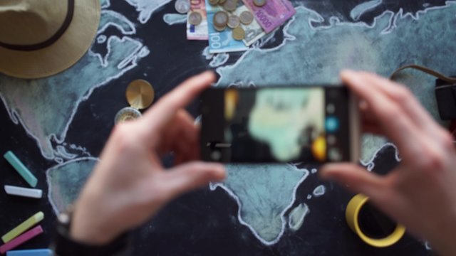 close up of woman with smartphone photographing map and travel stuff.