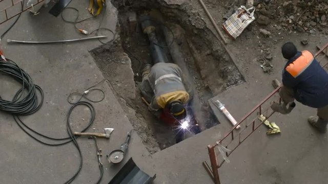 Welder Repairing a Pipe in a Hole