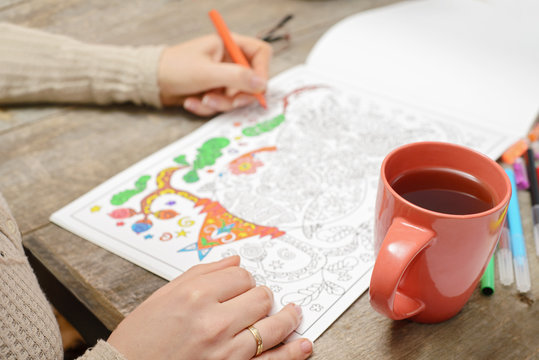 Woman coloring an adult coloring book and drinking tea, new stre