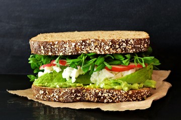 Superfood sandwich with avocado, egg whites, radish and pea shoots on whole grain bread against a slate background