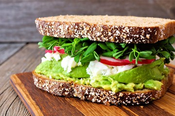 Superfood sandwich with whole grain bread, avocado, egg whites, radishes and pea shoots on wood board