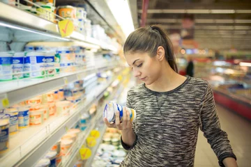  Young woman reading ingredients,declaration or expiration date on a diary product before buying it.Curious woman reading nutritional values of the food.Shopping in the supermarket grocery store. © eldarnurkovic