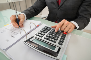 Close-up Of Businessman Calculating Invoice Using Calculator