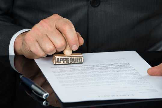 Close-up Of Businessman Hand Stamping On Approved Contract Form