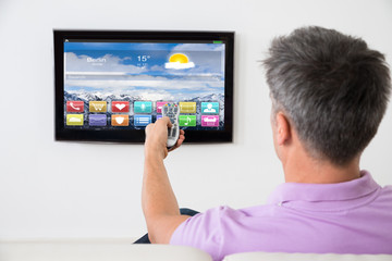 Man On Sofa Using Remote Control In Front Of TV