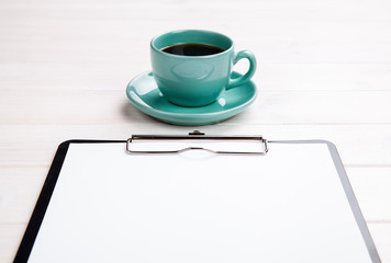Clipboard with blank page and cup of coffee on wooden desk. View from above.