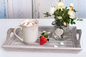Cup of hot chocolate with marshmallows, strawberry and hedge roses on the wooden tray