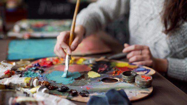 Closeup of paintbrush in woman hands mixing paints on palette
