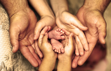 Руки отца, матери, дочери, держать ножки малыша. Дружелюбная счастливая семья, вместе