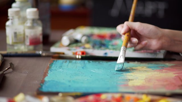 artist paints a picture of oil paint brush in hand with palette closeup.