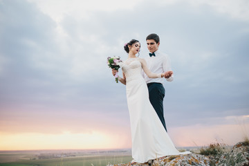 Beautiful wedding couple with bouquet flowers on the sunset