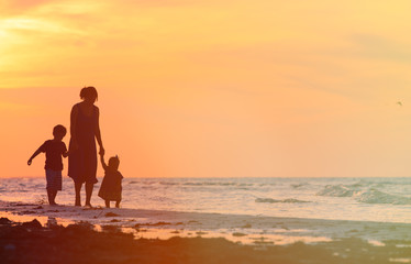 Fototapeta na wymiar mother and two kids walking at sunset beach