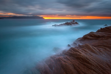 Waves and rocks in motion blur on coastline at sunrise