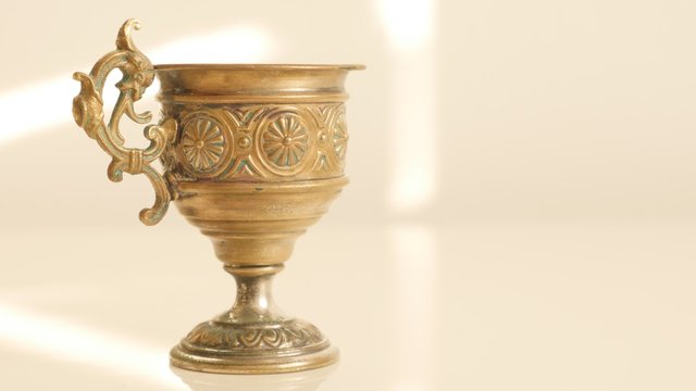 Aged holly grail look like object made of brass on white reflective surface 4K 2160p UltraHD footage - Slow tilt over patina brass grail on white surface 4K 3840X2160 UHD video 