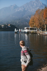 Fototapeta na wymiar man with a backpack and camera stands on the shore of a mountain lake Como