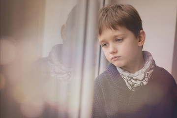 Sad thoughtful little boy looking through the window.