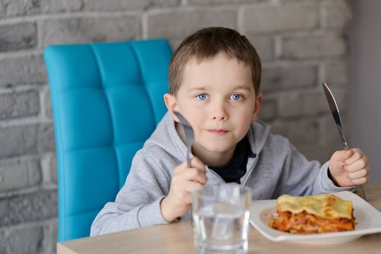 7 Years Old Boy Eating Lasagne In Dining Room