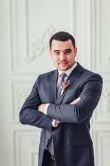 Handsome confident groom in a blue suit posing in the white stud