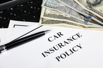 paper with the words "car insurance policy" rests on the keyboard with notes and pen