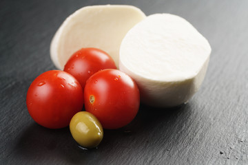 sliced mozarella ball with tomato and olives on slate background, shallow focus