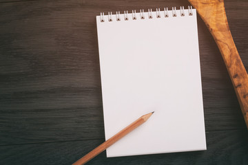 notepad with pencil and wood utensils on wood table, vintage toned