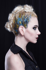 Young attractive blonde woman with creative hairstyle. She is rebellious, she has a colored mohawk with glitter and heavy makeup. Side view.