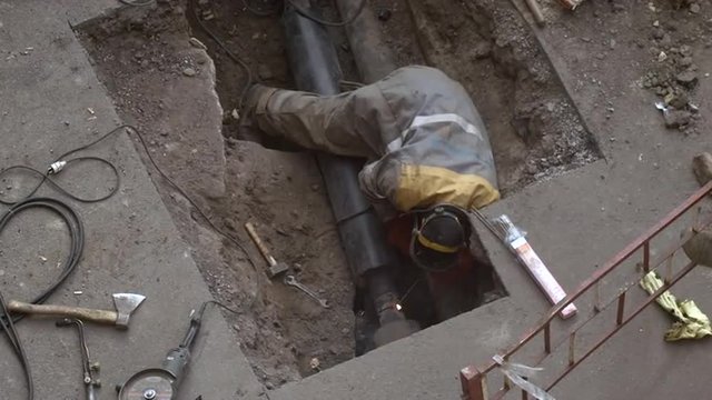 Welder Repairing a Pipe in a Hole