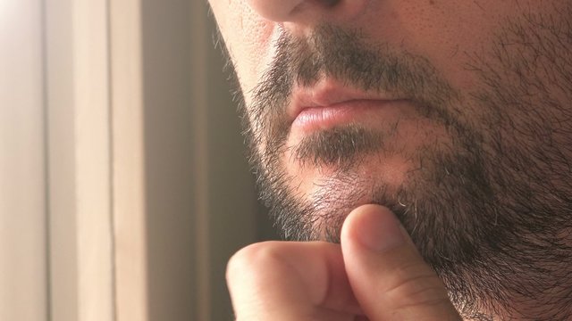 Close up of unshaven male thinking by the window, adult caucasian man contemplating.