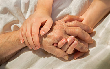 Fototapeta na wymiar hands of grandmother and grandchild in the bed