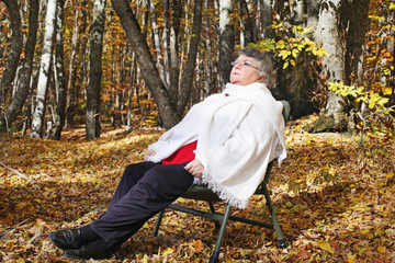Old woman is resting in forest in autumn