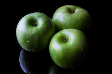 Three green fresh ripe apples on black background with reflection from high angle