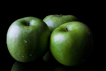 Three green fresh ripe apples on black background from side