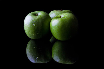 Three green fresh ripe apples on black background with reflection from side