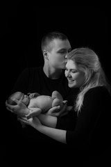 happy family , young parents holding a newborn baby in her arms and gently hugged him, black and white photo on a black background .