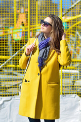 young brunette woman in a yellow coat and sunglasses looking at